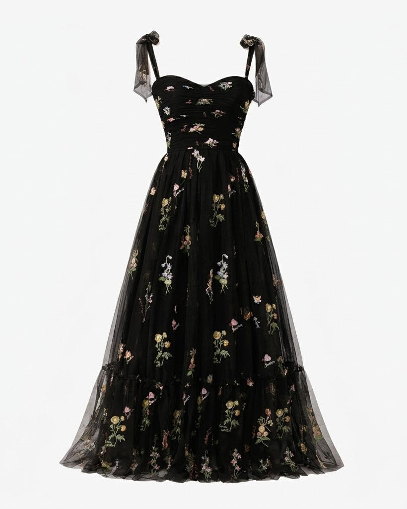 A black A-line evening gown with a floral print, featuring sheer black ribbon shoulder straps and a tiered tulle skirt, shown against a plain white background.