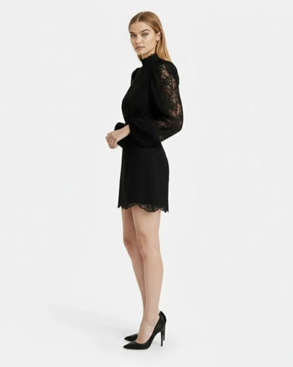 A woman modeling a black mini dress with long sheer lace sleeves and a black lace hem, paired with black high heels, against a plain white studio background.