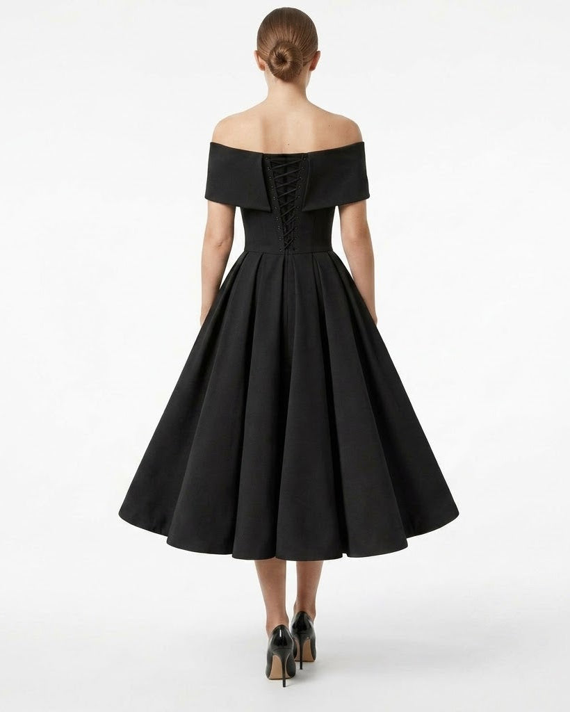 A woman viewed from the back wearing a black off-the-shoulder midi dress with a structured corset-style back and a full flared skirt, paired with black heels, against a plain white studio background.