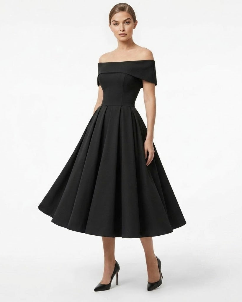 A woman modeling an off-the-shoulder black midi dress with a structured bodice and a full flared skirt, paired with black pointed-toe heels, against a plain white studio background.