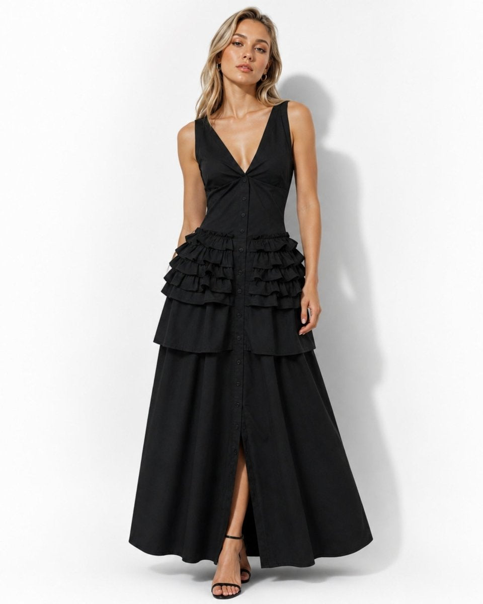 A woman modeling a sleeveless black maxi dress with a deep V-neckline, a twisted waist detail, a tiered ruffle waist, and a front slit, set against a plain white studio background.