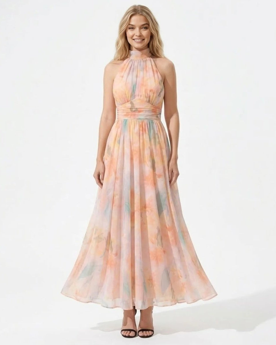 A woman modeling a sleeveless halter-neck maxi dress with a flowing chiffon-like skirt. The dress features a soft watercolor tie-dye pattern in pastel shades of peach, orange, pink, and light blue.