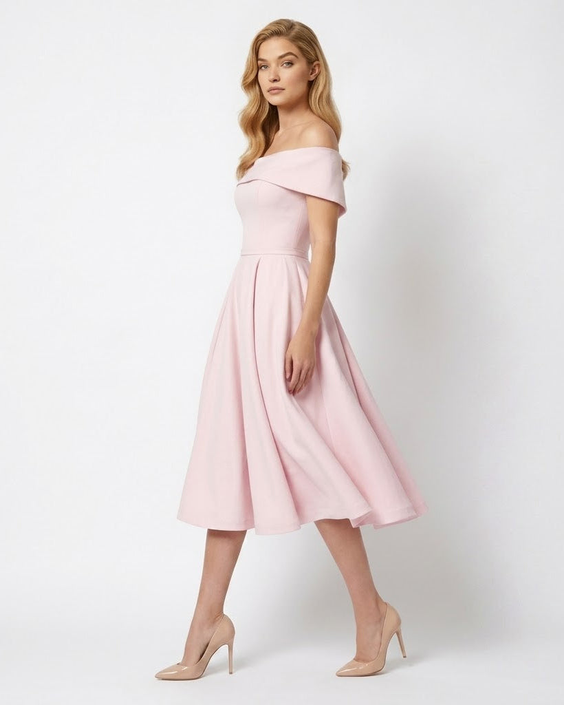 A woman modeling an off-the-shoulder midi dress in light pink with a flared skirt, paired with nude high heels, against a plain light gray studio background.