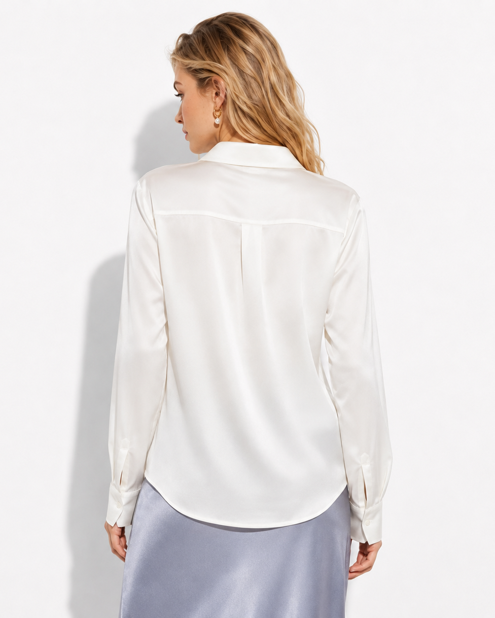 A woman viewed from the back wearing a white long-sleeve satin blouse and a light blue satin skirt, set against a plain white studio background.