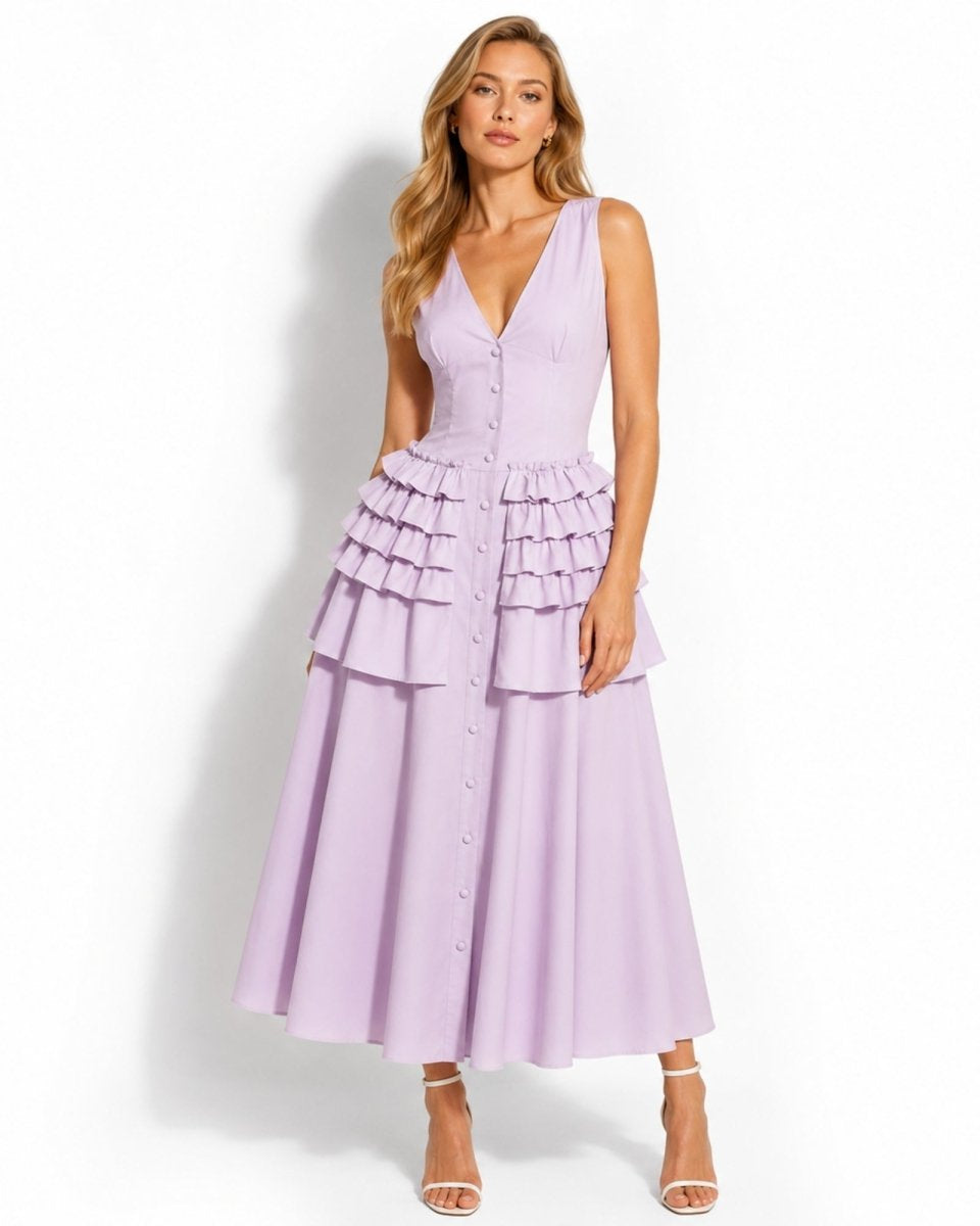A woman modeling a sleeveless lavender midi dress with a deep V-neckline, button-front bodice, and tiered ruffle detail at the waist, paired with white heeled sandals against a plain white studio background.