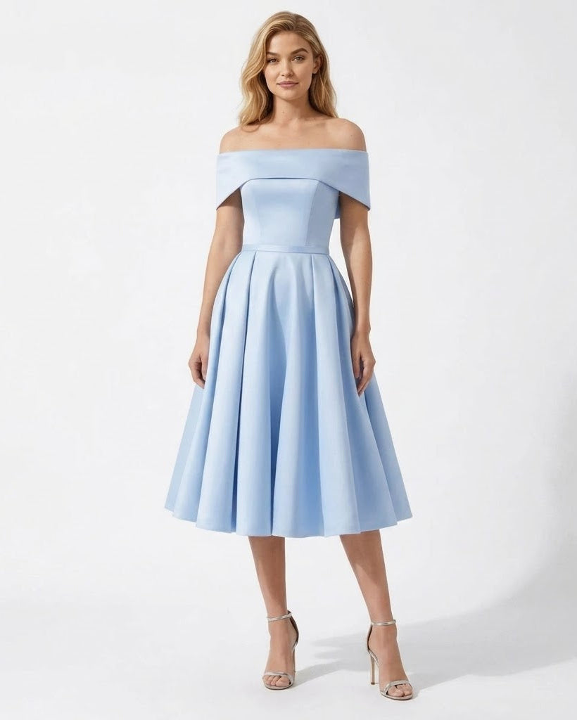 A woman modeling an off-the-shoulder light blue midi dress with a structured bodice and flared skirt, paired with clear high-heeled sandals, against a plain white studio background.