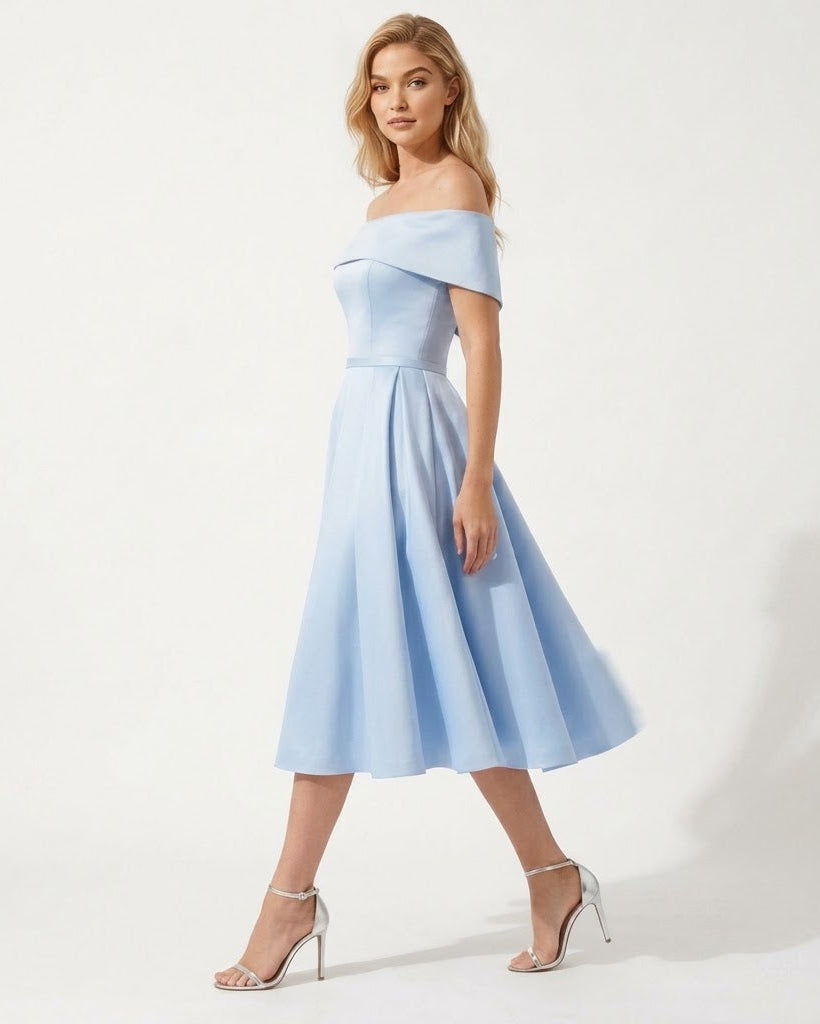 A woman modeling an off-the-shoulder light blue midi dress with a structured bodice and flared skirt, paired with clear high-heeled sandals, against a plain white studio background.