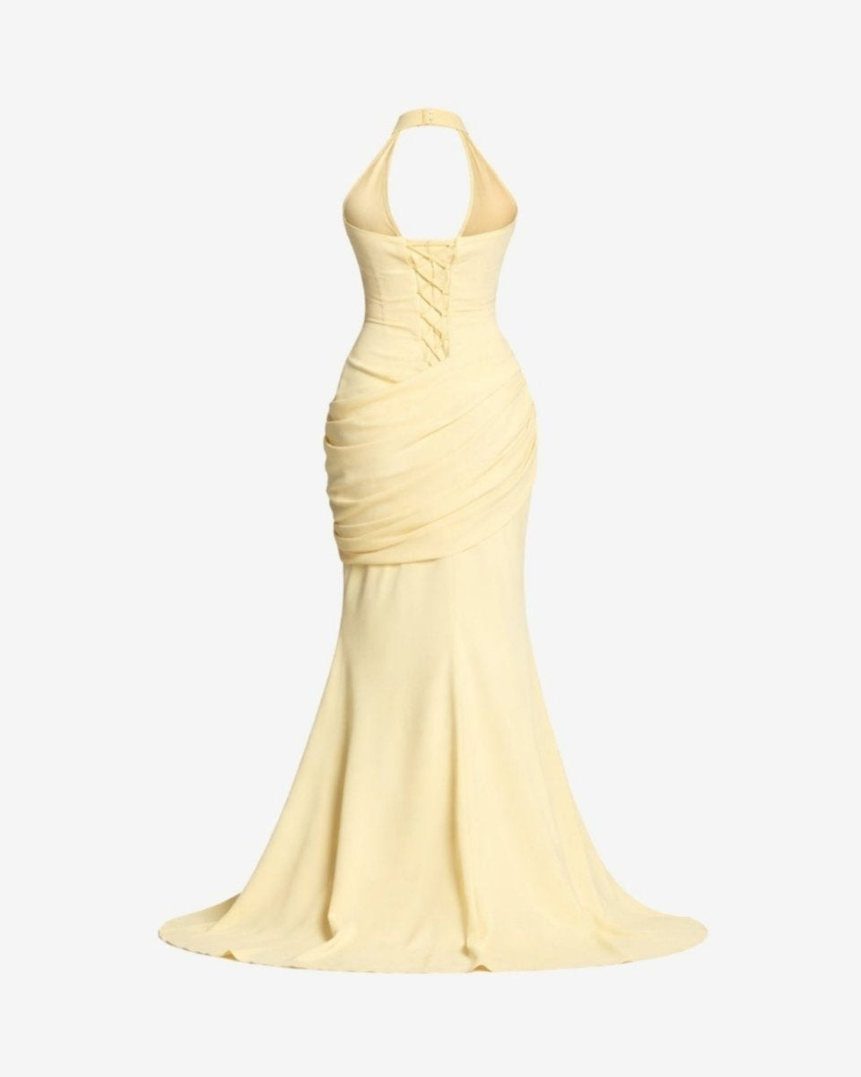 A pale yellow halter-neck mermaid gown with ruched draping at the waist, shown on a plain light gray background.
