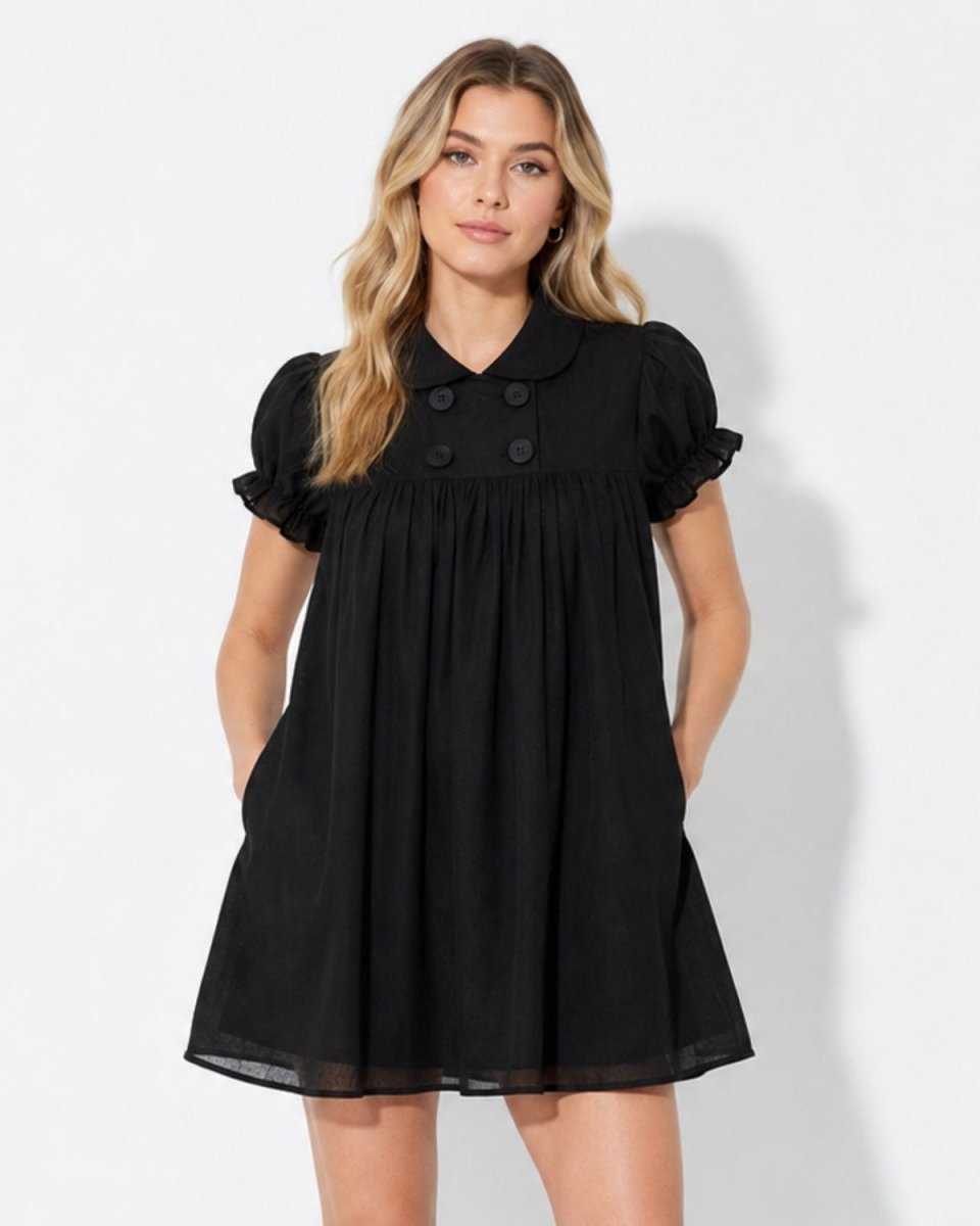 Woman with hands in pockets wearing the Ondara black puff sleeve babydoll mini dress featuring a Peter Pan collar against a white studio background.
