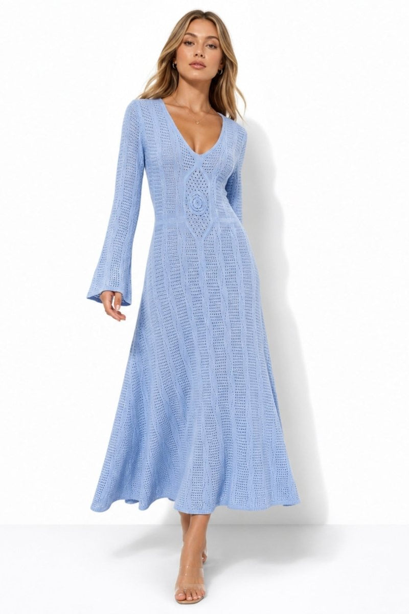 A woman modeling a light blue long-sleeve maxi dress with a textured crochet pattern and a deep V-neckline, set against a plain white studio background.