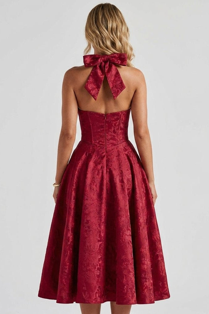 Back view of the burgundy red open back midi dress, featuring a dramatic oversized halter bow and tailored corset waist.