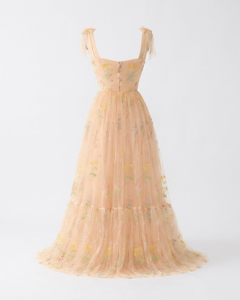 A peach-colored sleeveless tulle maxi dress with delicate floral embroidery and tie straps, displayed on a clean white background.