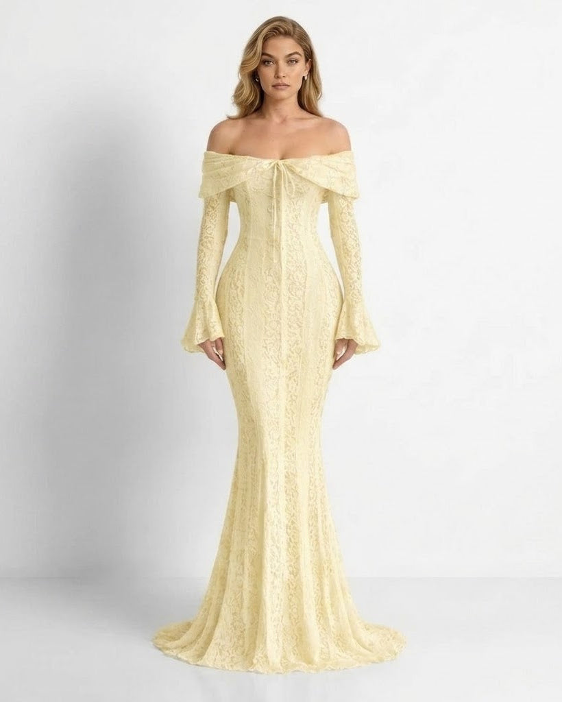 A woman modeling an off-the-shoulder, long-sleeved lace gown in a pale yellow color, standing against a light gray studio background.