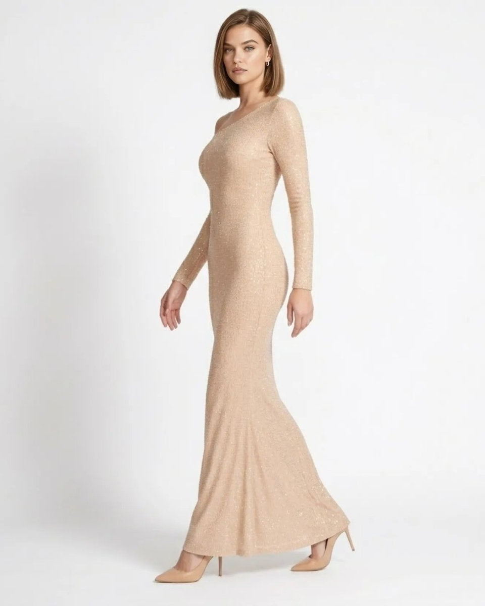 A woman modeling a long-sleeve, bodycon maxi dress in a shimmering champagne beige color, paired with matching pointed-toe heels, against a plain white studio background.