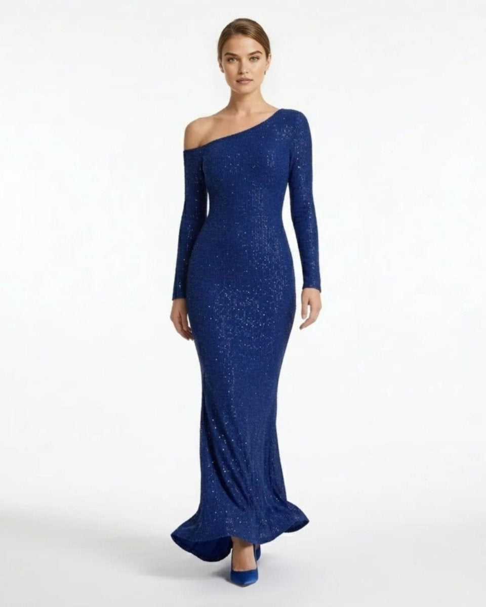 A woman modeling a long-sleeve, one-shoulder floor-length gown in a rich royal blue with subtle shimmering texture, set against a plain white studio background.