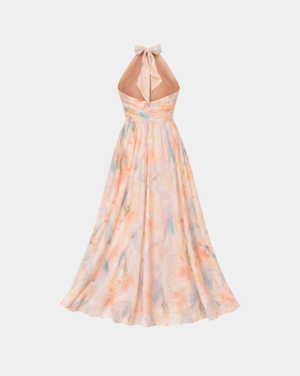 Woman wearing Ondara luxury pastel watercolor floral halter maxi dress standing in an elegant garden.