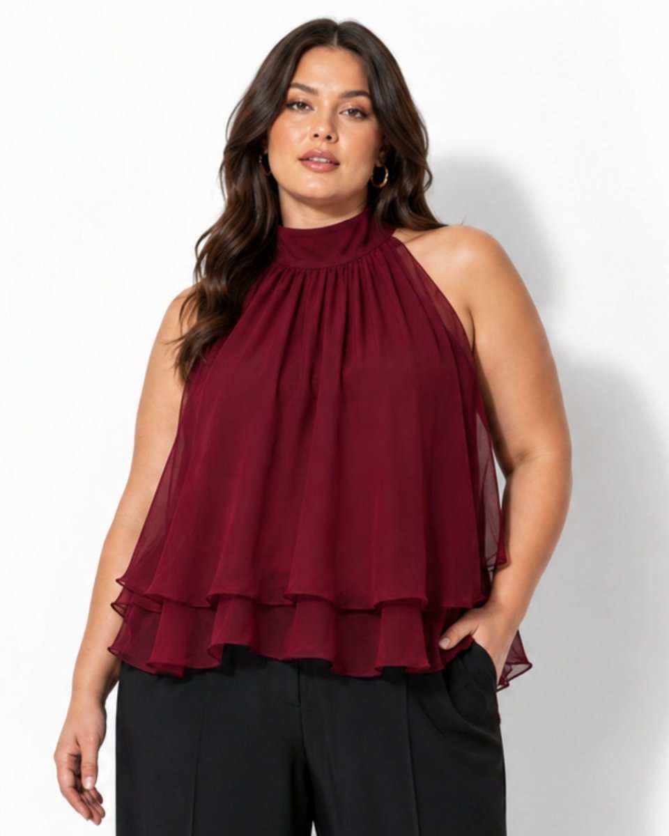 Plus size model showcasing the flattering drape of the Ondara burgundy red chiffon tiered halter blouse with hands in pockets.