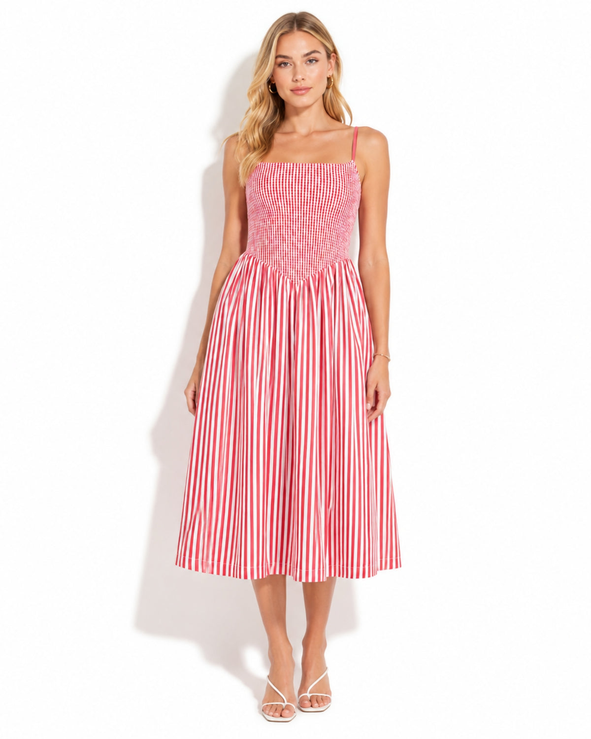 A woman modeling a sleeveless midi dress with a smocked bodice and red-and-white vertical stripes, standing against a plain white studio background.