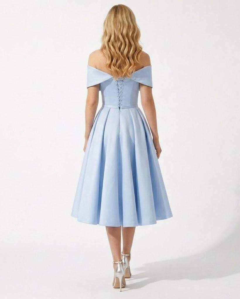 A woman viewed from behind wearing a light blue off-the-shoulder midi dress with a structured lace-up back and flared skirt, paired with metallic high heels, against a plain white studio background.