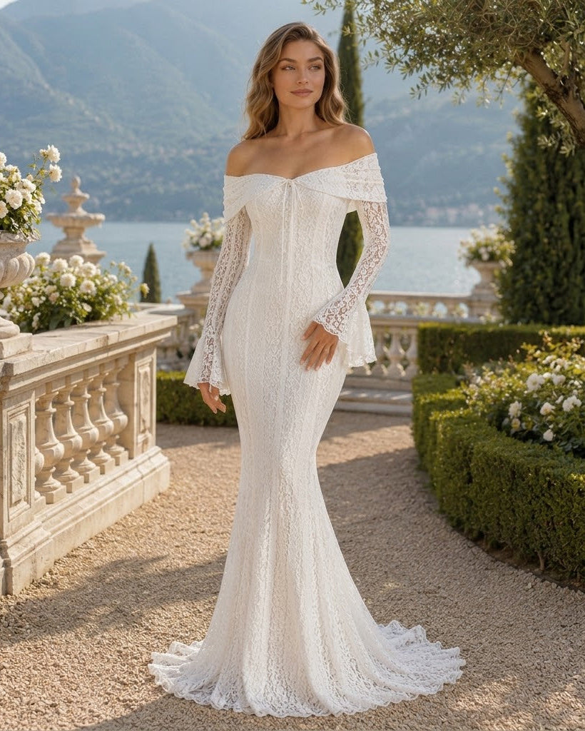 An off-the-shoulder lace mermaid-style wedding gown with long sheer lace sleeves, worn by a woman standing in a formal garden courtyard with stone balustrades, flowers, and water in the background.