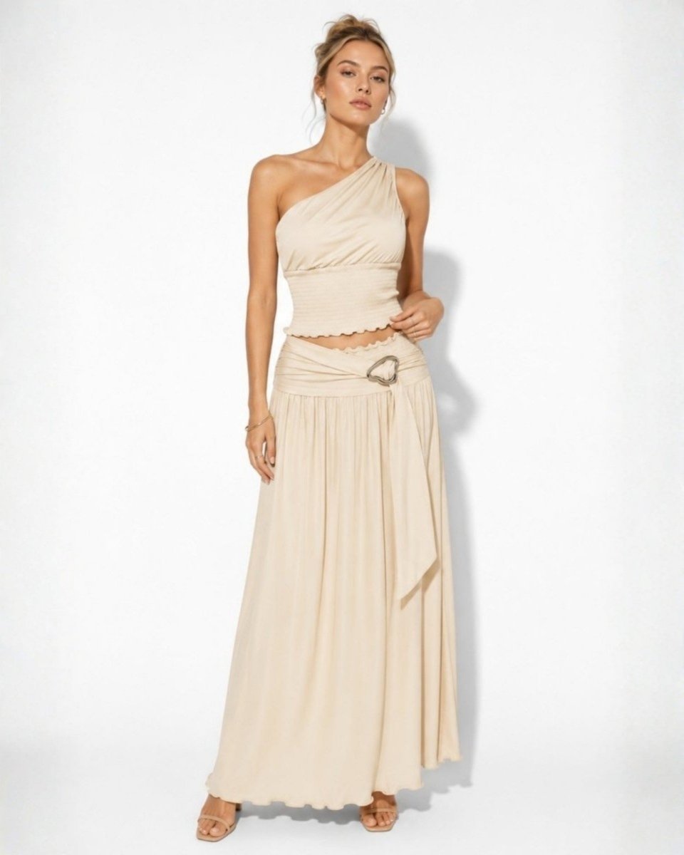 Front view of woman wearing Ondara luxury beige two-piece maxi skirt set with one-shoulder smocked top.