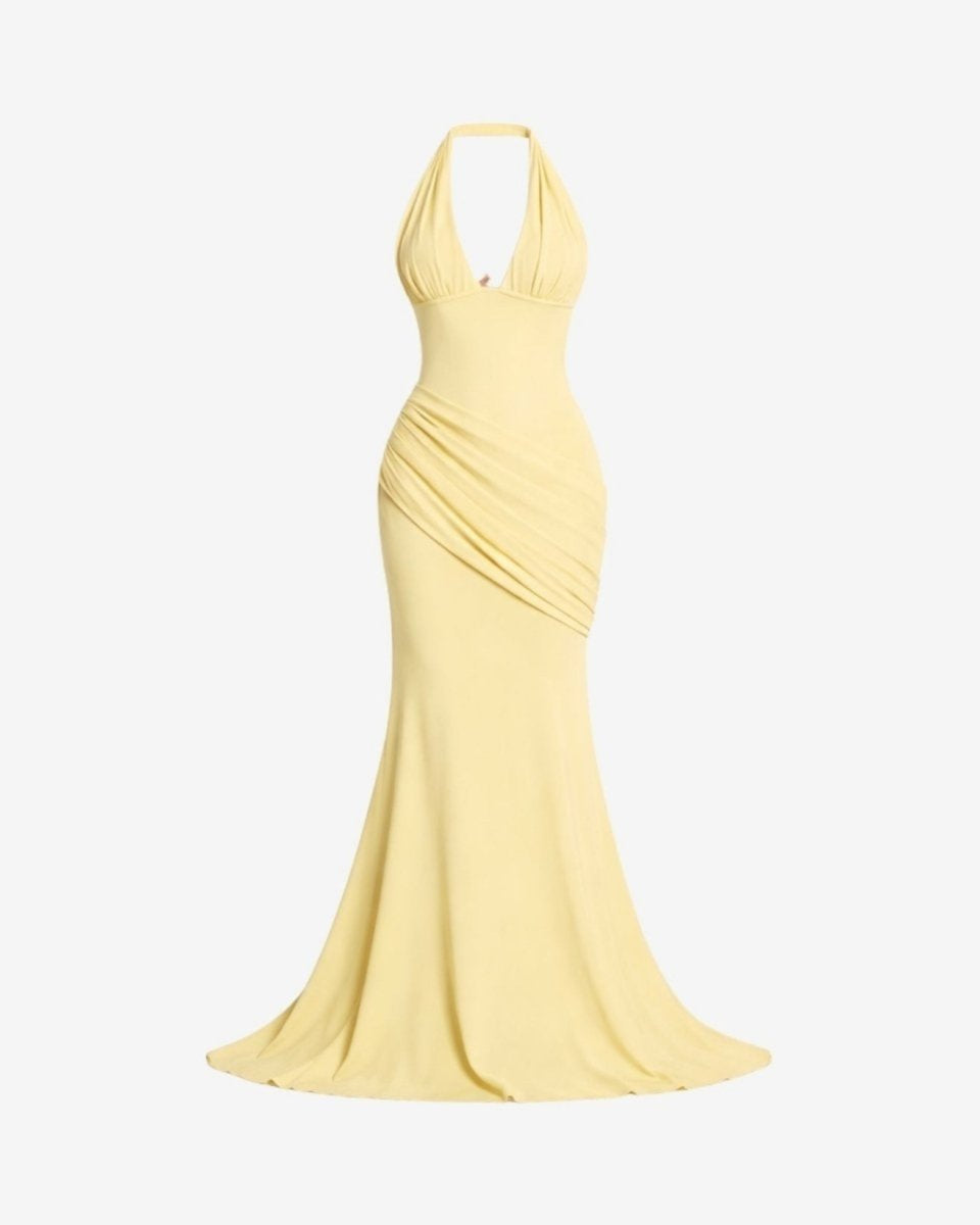 A pale yellow halter-neck maxi dress with a fitted silhouette and draped ruching at the waist, shown against a plain light gray background.